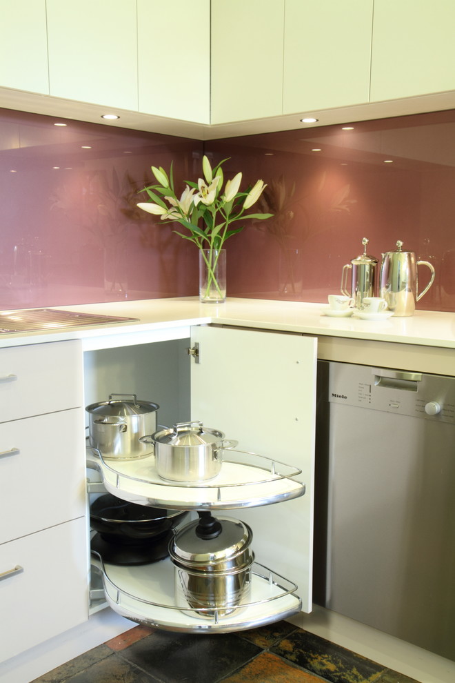 Mid-sized contemporary u-shaped separate kitchen in Sydney with flat-panel cabinets, white cabinets, quartz benchtops, glass sheet splashback, stainless steel appliances, terra-cotta floors, a double-bowl sink and pink splashback.