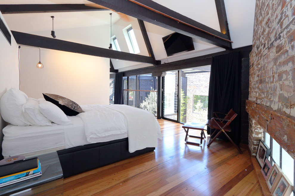 This is an example of a mid-sized industrial master bedroom in Sydney with white walls and medium hardwood floors.