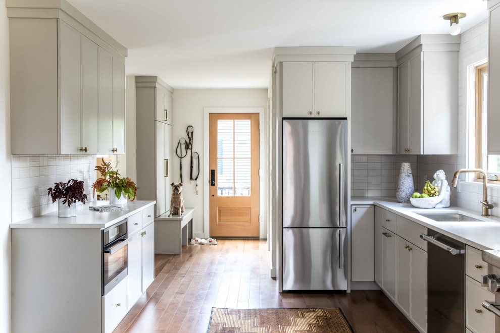 Inspiration for a mid-sized transitional galley eat-in kitchen in Portland Maine with an undermount sink, shaker cabinets, grey cabinets, quartz benchtops, white splashback, ceramic splashback, stainless steel appliances, light hardwood floors, no island and grey benchtop.
