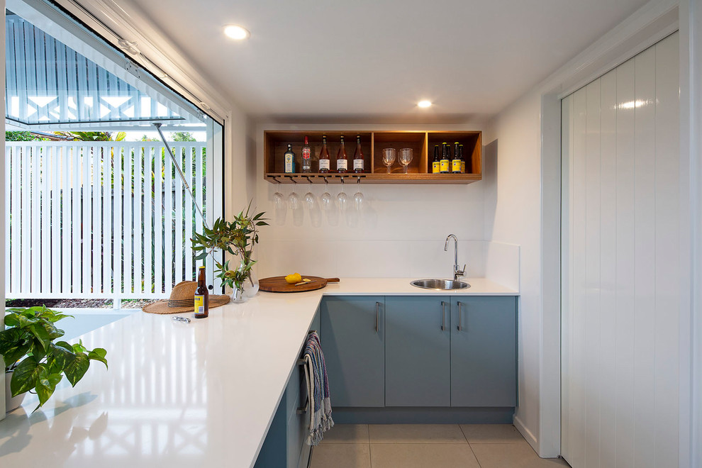 This is an example of a beach style l-shaped seated home bar in Sunshine Coast with blue cabinets, quartz benchtops, white splashback, ceramic splashback, concrete floors, grey floor, white benchtop, a drop-in sink and flat-panel cabinets.