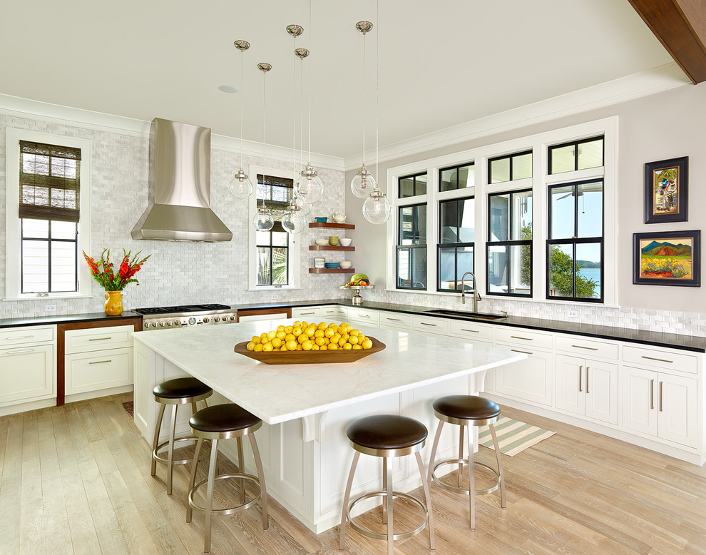 Design ideas for a beach style l-shaped kitchen in Charleston with an undermount sink, shaker cabinets, white cabinets, white splashback, mosaic tile splashback, stainless steel appliances, light hardwood floors and with island.