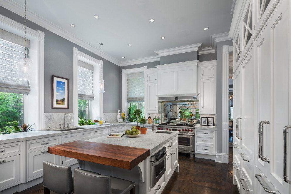 Photo of a traditional u-shaped kitchen in Chicago with an undermount sink, recessed-panel cabinets, white cabinets, mirror splashback, stainless steel appliances, dark hardwood floors and with island.