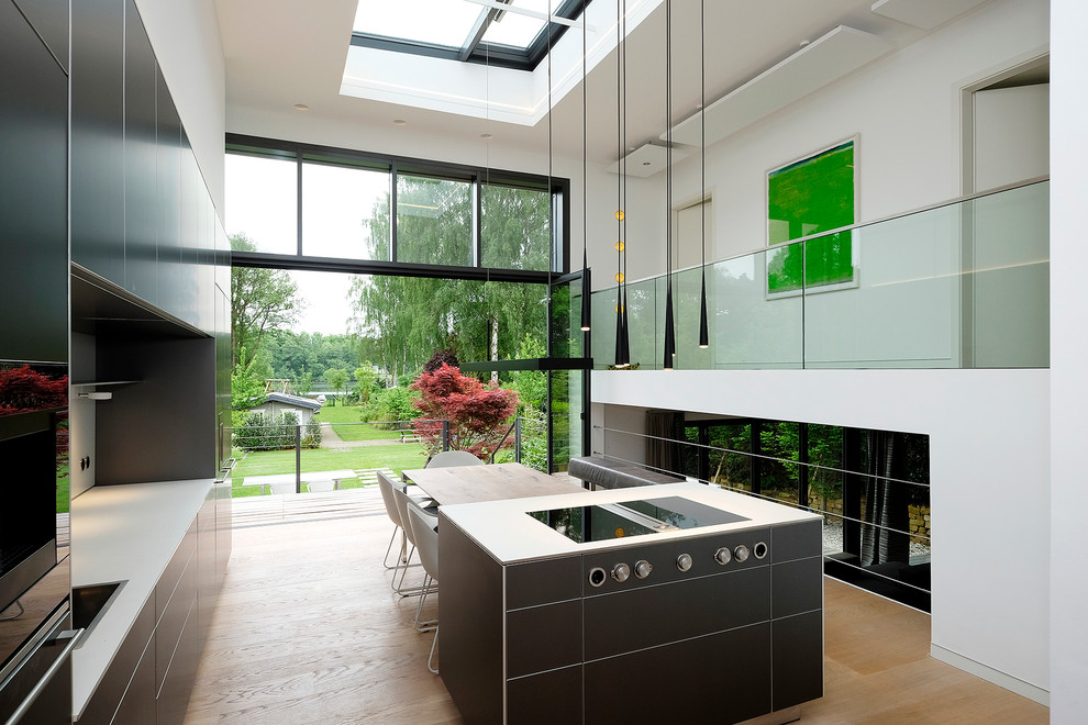 Inspiration for a contemporary single-wall open plan kitchen in Hamburg with flat-panel cabinets, black cabinets, black appliances, light hardwood floors and with island.