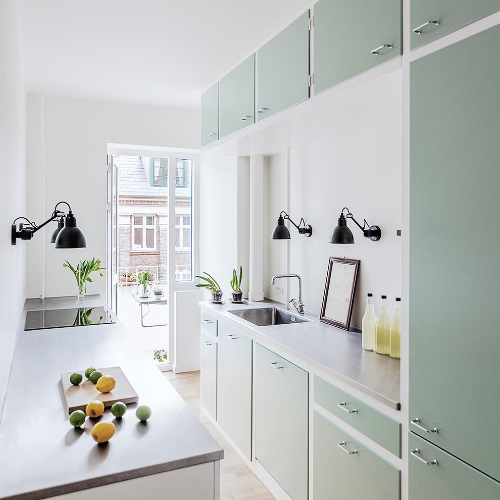 Inspiration for a scandinavian galley separate kitchen in Copenhagen with an integrated sink, flat-panel cabinets, green cabinets, concrete benchtops, grey splashback, light hardwood floors, no island and beige floor.