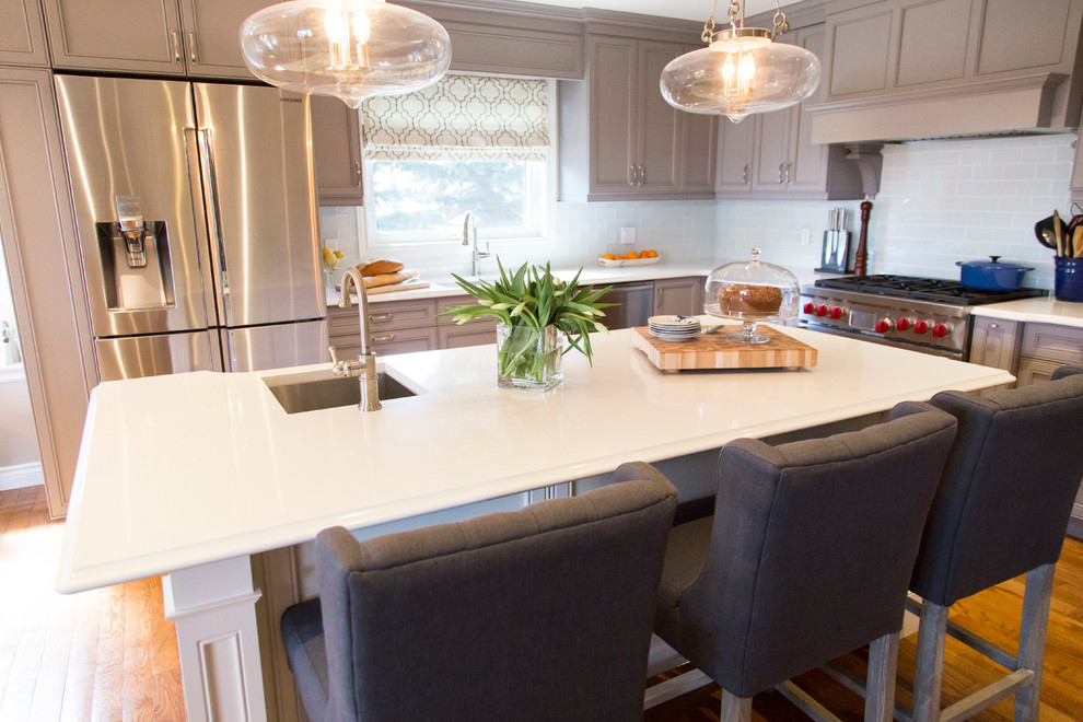 Inspiration for a mid-sized transitional u-shaped medium tone wood floor open concept kitchen remodel in Toronto with an undermount sink, recessed-panel cabinets, gray cabinets, quartzite countertops, white backsplash, stainless steel appliances and an island
