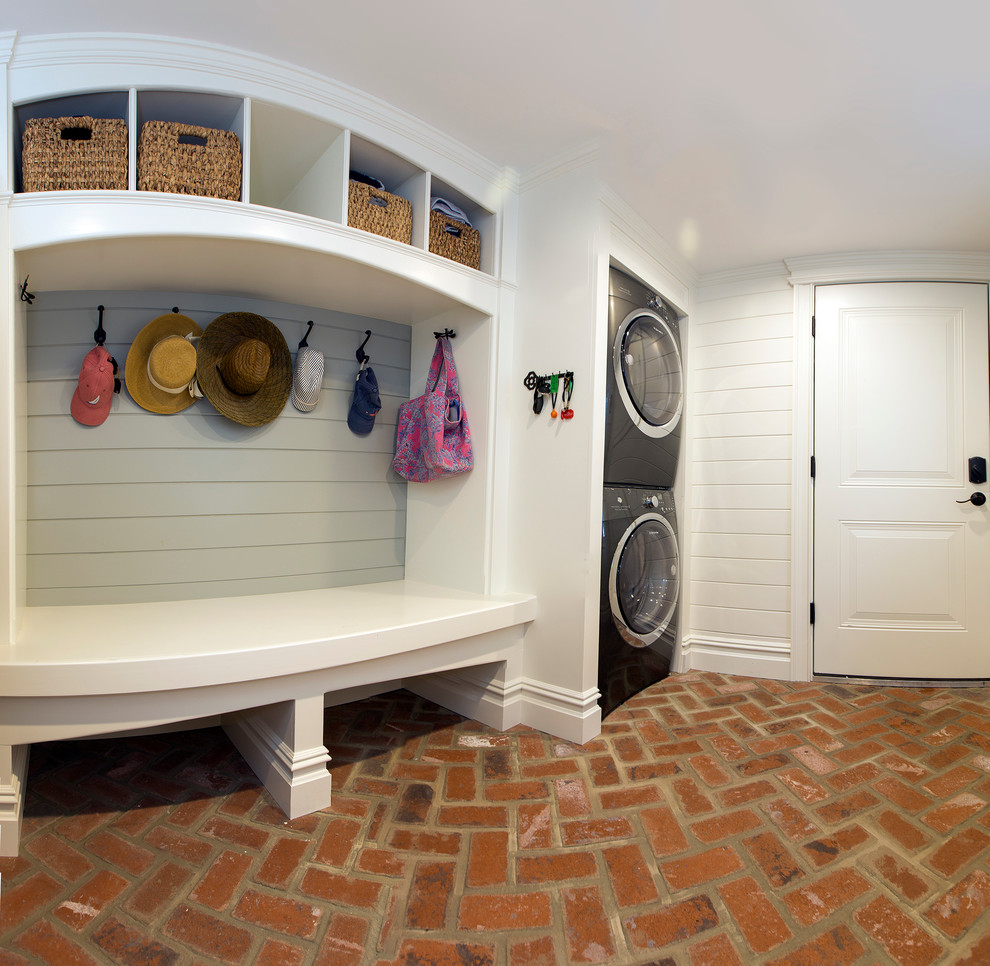 Inspiration for a large beach style galley utility room in New York with open cabinets, white cabinets, white walls, brick floors and a stacked washer and dryer.