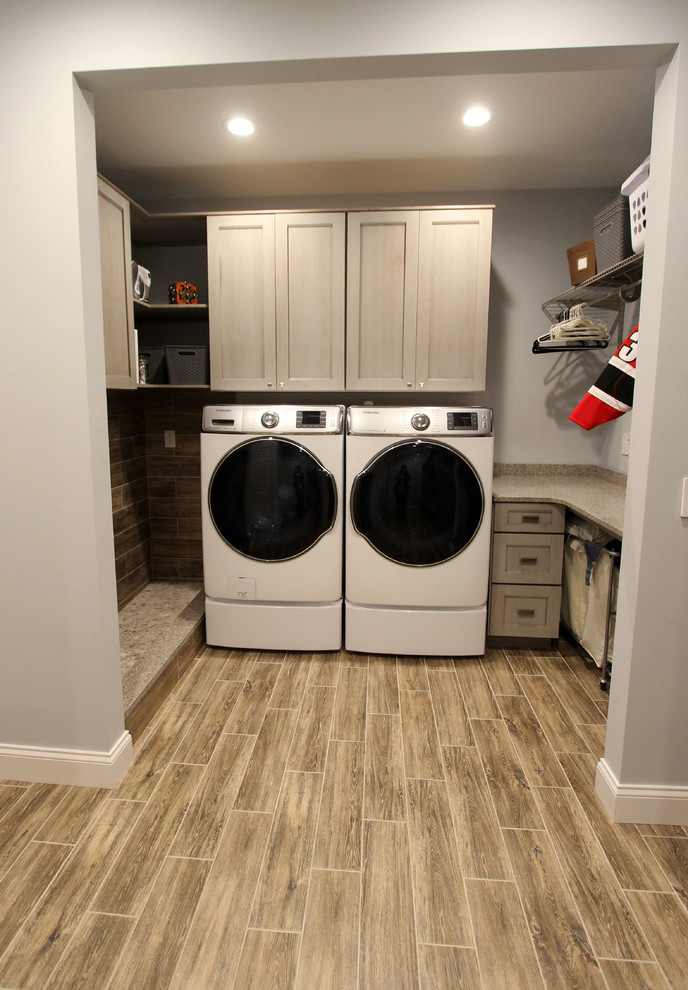Photo of a mid-sized transitional galley utility room in Cleveland with flat-panel cabinets, grey cabinets, quartz benchtops, grey walls, laminate floors, a side-by-side washer and dryer and brown floor.