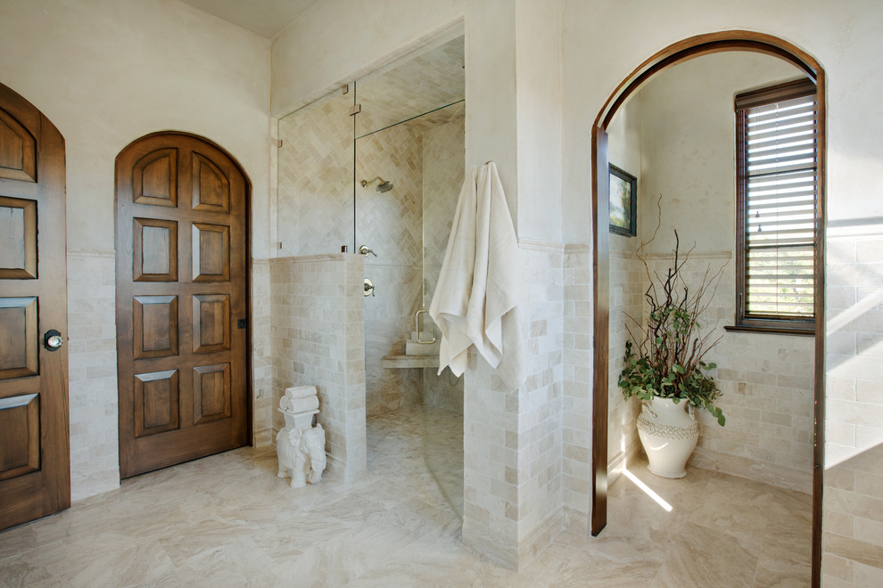 Photo of a mediterranean master bathroom in Other with a curbless shower, beige tile, marble, beige walls, marble floors, beige floor, a hinged shower door, beaded inset cabinets, beige cabinets, a freestanding tub, an undermount sink and marble benchtops.