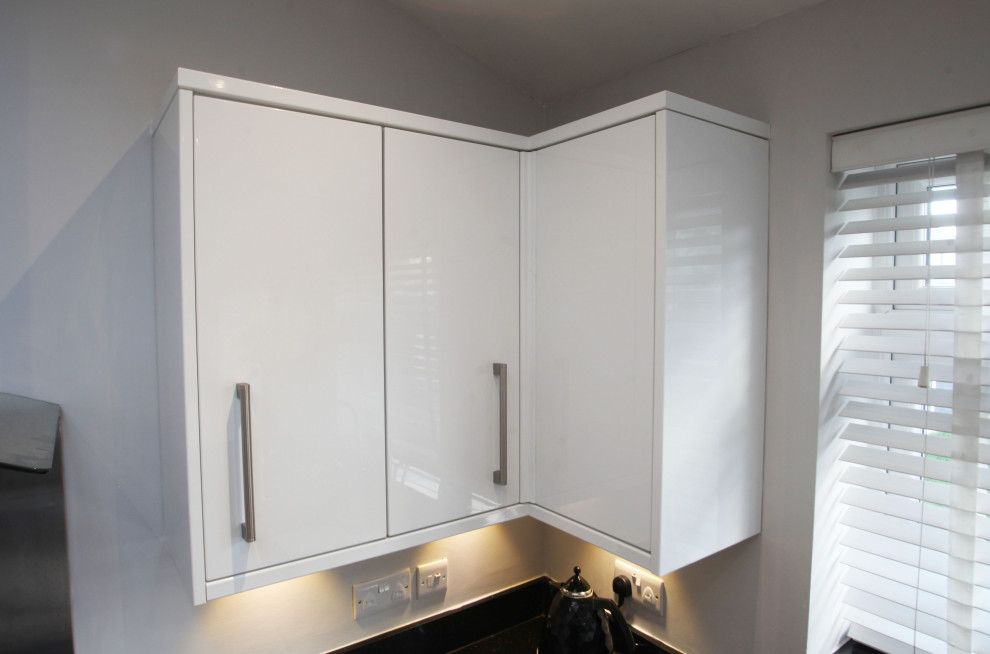 Photo of a medium sized modern l-shaped open plan kitchen in Cheshire with a double-bowl sink, flat-panel cabinets, white cabinets, granite worktops, metallic splashback, metal splashback, black appliances, porcelain flooring, a breakfast bar, beige floors and black worktops.