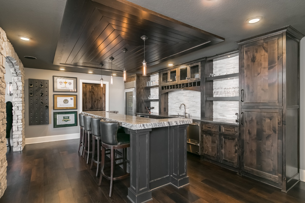 Inspiration for a large modern single-wall seated home bar in Minneapolis with an undermount sink, shaker cabinets, distressed cabinets, granite benchtops, white splashback, matchstick tile splashback, dark hardwood floors, brown floor and white benchtop.