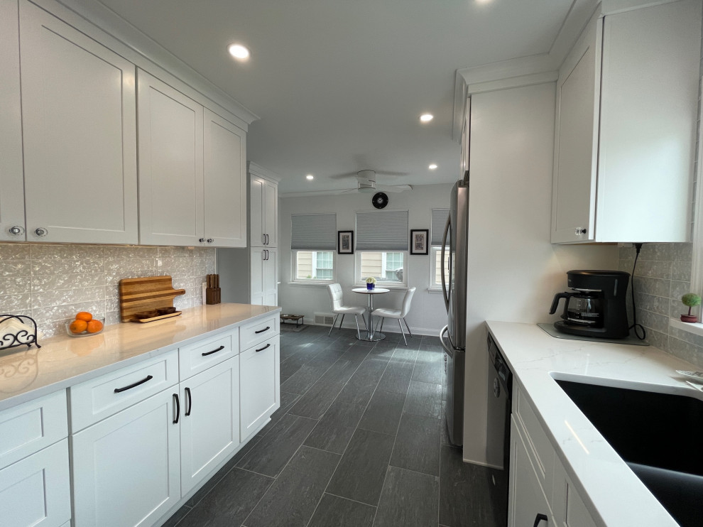 Photo of a medium sized modern galley kitchen/diner in New York with a submerged sink, shaker cabinets, white cabinets, engineered stone countertops, white splashback, glass tiled splashback, stainless steel appliances, porcelain flooring, no island, grey floors and white worktops.