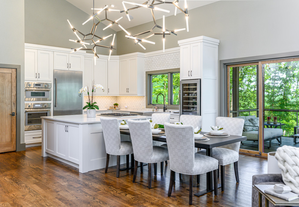 Inspiration for a large transitional l-shaped eat-in kitchen in Other with a farmhouse sink, shaker cabinets, white cabinets, white splashback, stainless steel appliances, dark hardwood floors, with island, brown floor, white benchtop, quartzite benchtops and mosaic tile splashback.