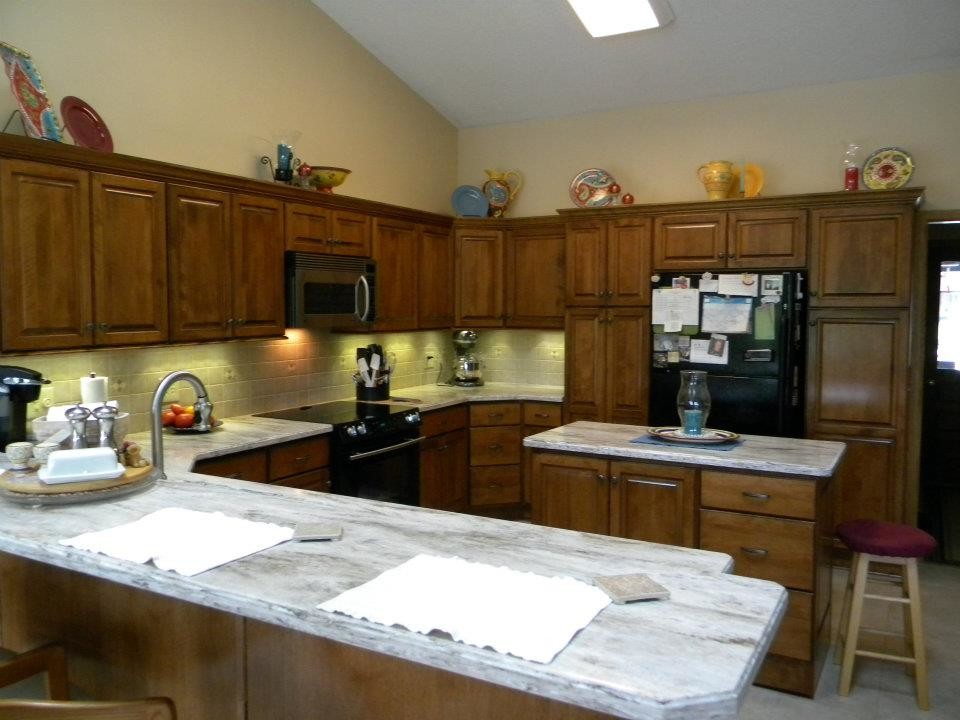 Inspiration for a large timeless l-shaped eat-in kitchen remodel with an undermount sink, raised-panel cabinets, medium tone wood cabinets, marble countertops, beige backsplash, ceramic backsplash, black appliances and an island