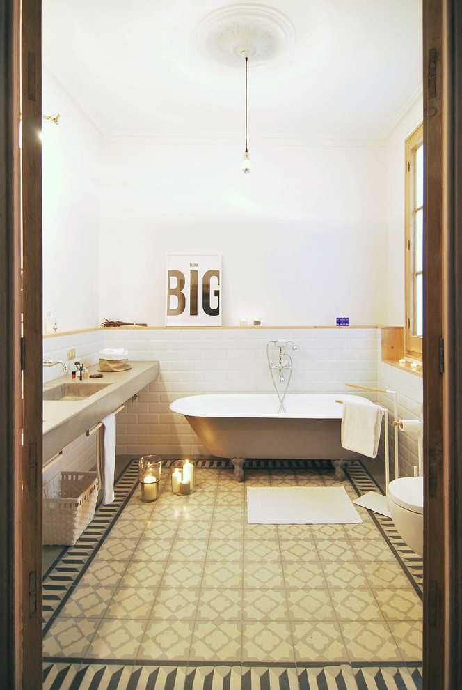 Design ideas for a mid-sized mediterranean 3/4 bathroom in Barcelona with a claw-foot tub, white tile, white walls, a one-piece toilet, mosaic tile floors, an integrated sink, concrete benchtops and a shower/bathtub combo.