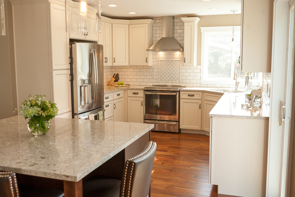 Example of a mid-sized transitional u-shaped dark wood floor open concept kitchen design with an undermount sink, raised-panel cabinets, white cabinets, quartzite countertops, white backsplash, subway tile backsplash, stainless steel appliances and an island
