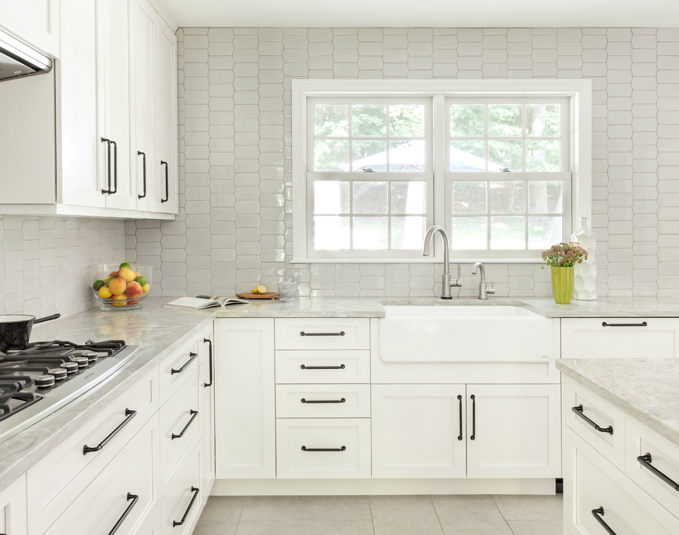 Inspiration for a mid-sized transitional l-shaped separate kitchen in New York with shaker cabinets, white cabinets, quartzite benchtops, porcelain floors, a farmhouse sink, grey splashback, ceramic splashback, stainless steel appliances, with island, beige floor and grey benchtop.