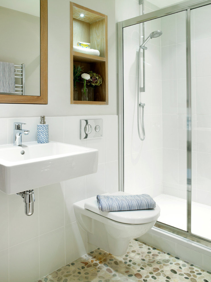 Photo of a small transitional bathroom in London with a wall-mount sink, an alcove shower, a wall-mount toilet, white tile, ceramic tile, white walls and pebble tile floors.