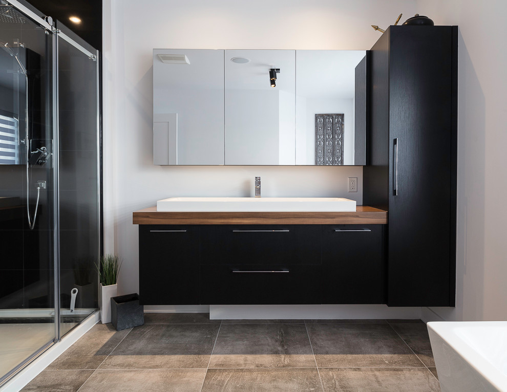 This is an example of a mid-sized contemporary master wet room bathroom in Montreal with flat-panel cabinets, black cabinets, a japanese tub, black tile, ceramic tile, grey walls, a vessel sink, laminate benchtops, grey floor and a sliding shower screen.