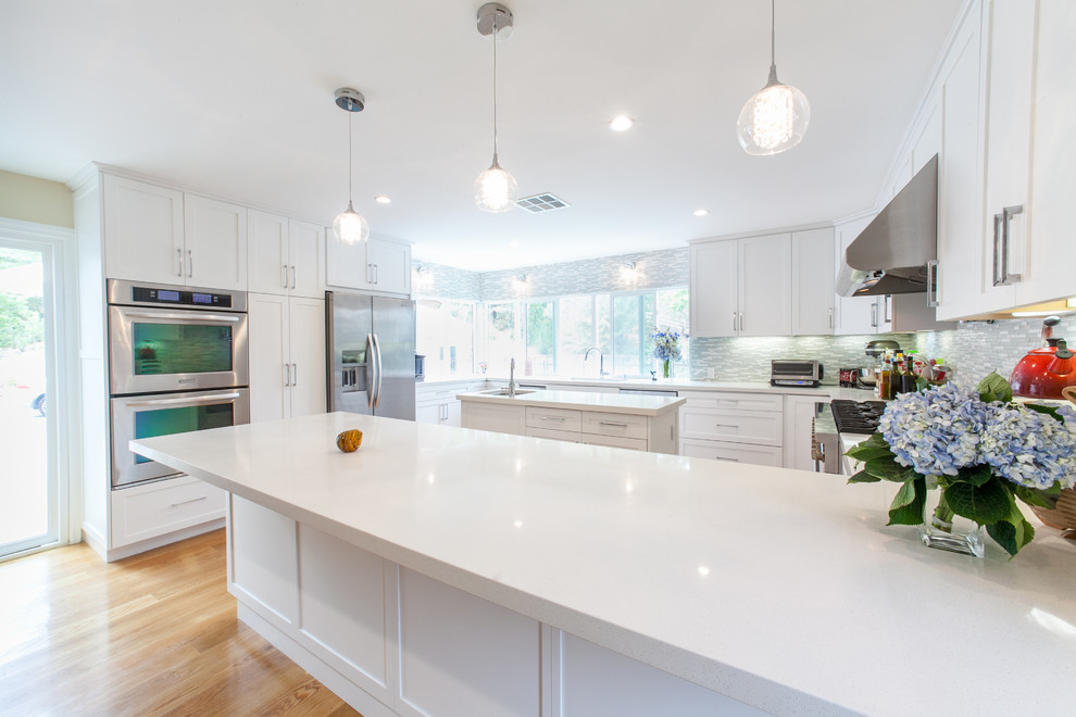 Expansive contemporary u-shaped eat-in kitchen in Los Angeles with an undermount sink, flat-panel cabinets, white cabinets, quartz benchtops, green splashback, glass tile splashback, stainless steel appliances, light hardwood floors and multiple islands.