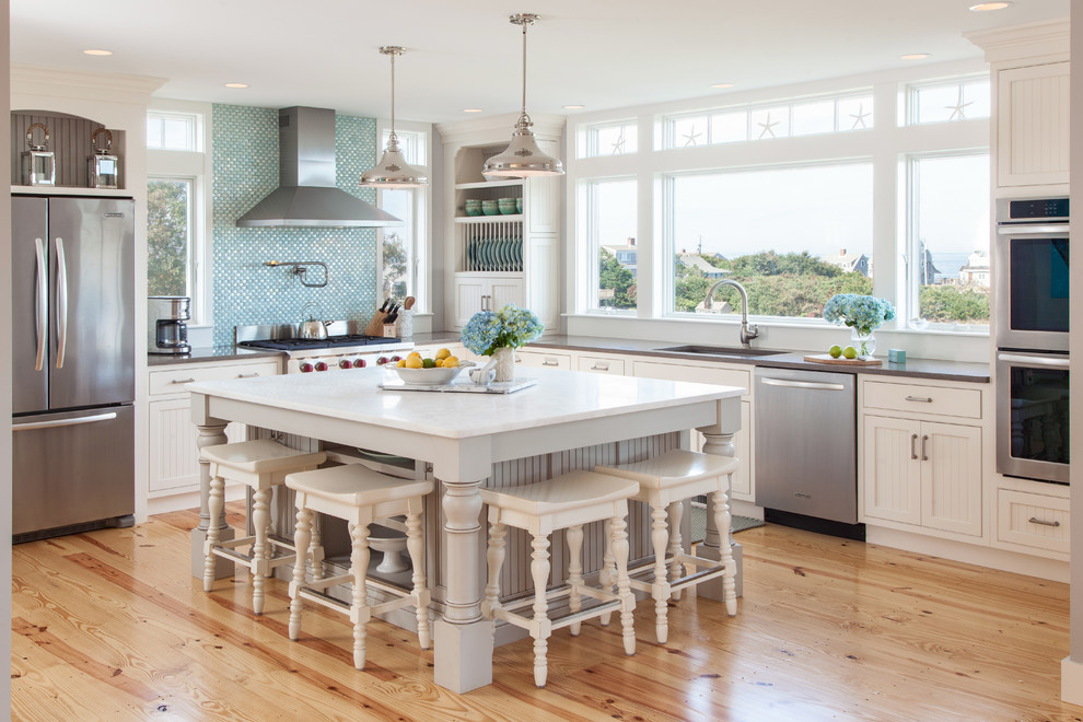 Inspiration for a large beach style l-shaped eat-in kitchen in Boston with an integrated sink, recessed-panel cabinets, white cabinets, solid surface benchtops, blue splashback, mosaic tile splashback, stainless steel appliances, medium hardwood floors and with island.