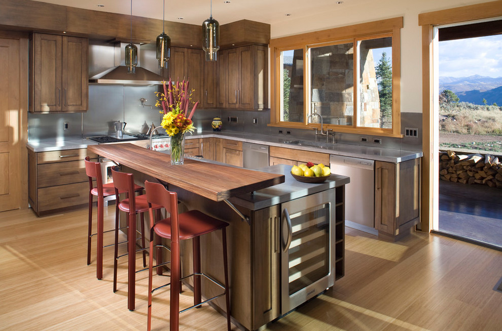 Photo of a country l-shaped kitchen in New York with an integrated sink, shaker cabinets, dark wood cabinets, metallic splashback, stainless steel appliances, light hardwood floors and with island.