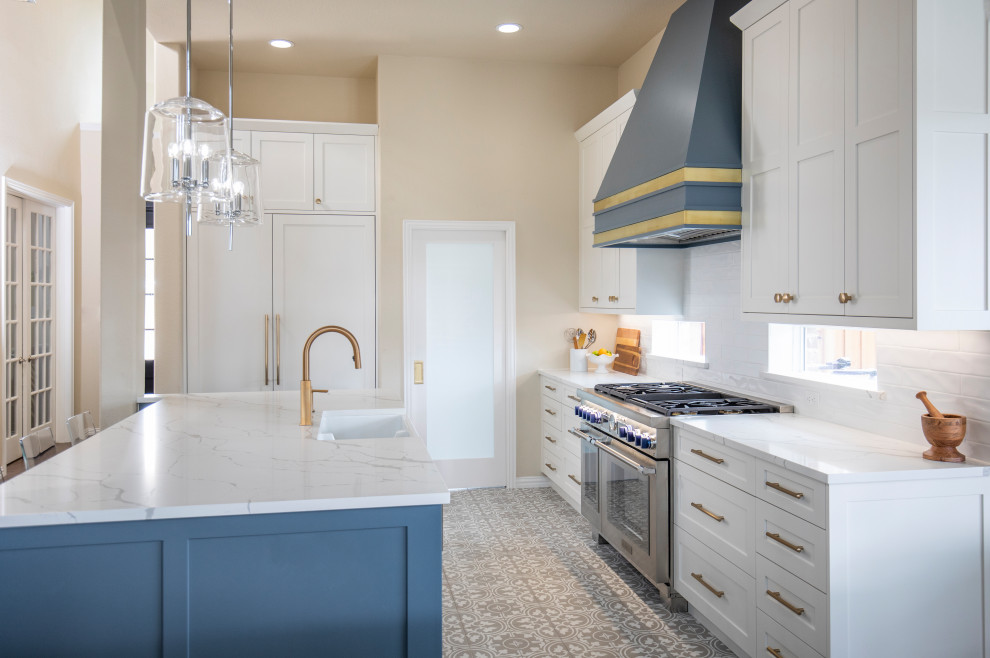 This is an example of a large transitional l-shaped eat-in kitchen in Dallas with a farmhouse sink, shaker cabinets, white cabinets, quartz benchtops, white splashback, subway tile splashback, stainless steel appliances, porcelain floors, with island, multi-coloured floor and white benchtop.