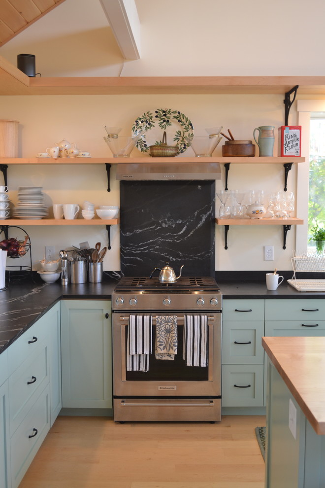Inspiration for a country l-shaped separate kitchen in Burlington with a farmhouse sink, shaker cabinets, black splashback, stone slab splashback, stainless steel appliances, light hardwood floors, with island, blue cabinets, soapstone benchtops and brown floor.