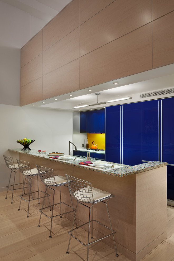 Photo of a contemporary galley open plan kitchen in New York with a drop-in sink, glass-front cabinets, blue cabinets, recycled glass benchtops, glass sheet splashback and coloured appliances.