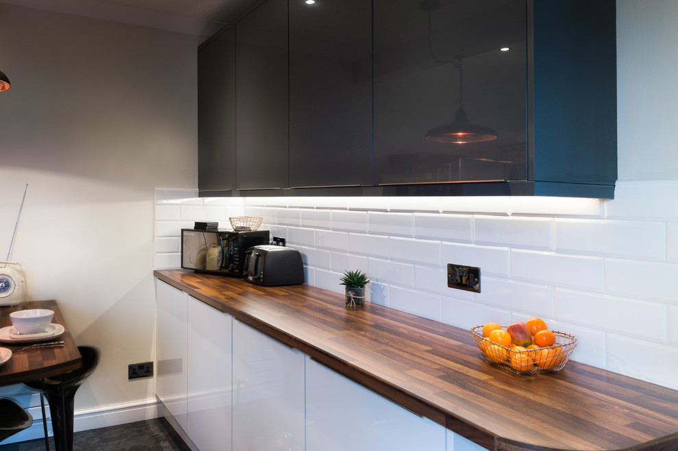 Photo of a mid-sized modern u-shaped separate kitchen in Cornwall with an integrated sink, glass-front cabinets, white cabinets, wood benchtops, white splashback, cement tile splashback, limestone floors, with island, black floor and brown benchtop.