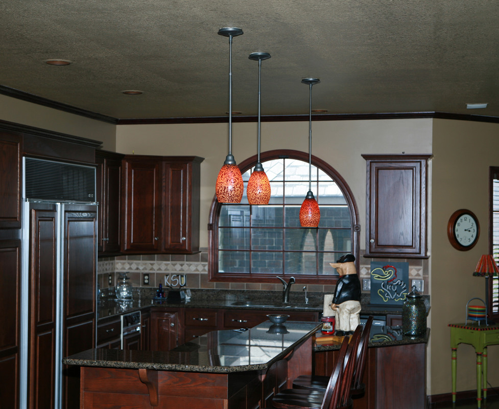 Example of a large transitional l-shaped porcelain tile eat-in kitchen design in Wichita with an undermount sink, raised-panel cabinets, dark wood cabinets, granite countertops, brown backsplash, porcelain backsplash, paneled appliances and a peninsula