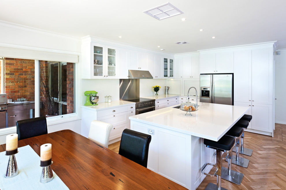 Transitional l-shaped open plan kitchen in Melbourne with shaker cabinets, white cabinets, stainless steel appliances and white splashback.