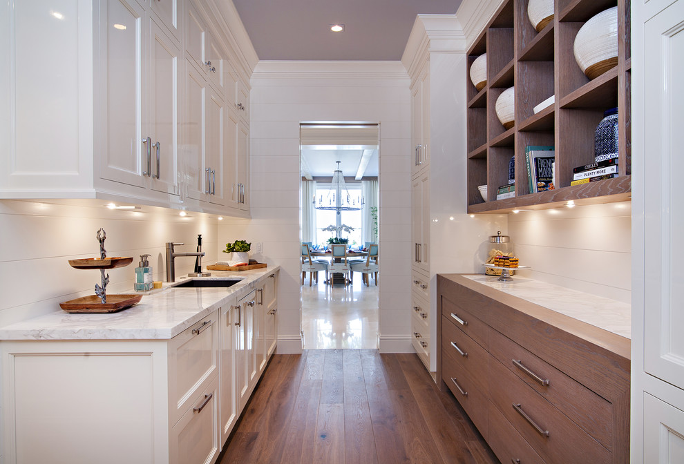 Photo of an expansive transitional kitchen pantry in Miami with an undermount sink, shaker cabinets, white cabinets, marble benchtops, white splashback, stone slab splashback, white appliances, medium hardwood floors and with island.