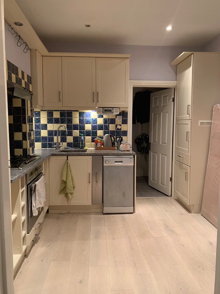 Photo of a small contemporary l-shaped eat-in kitchen in London with a drop-in sink, flat-panel cabinets, grey cabinets, quartzite benchtops, grey splashback, stone slab splashback, black appliances, light hardwood floors, no island and grey benchtop.