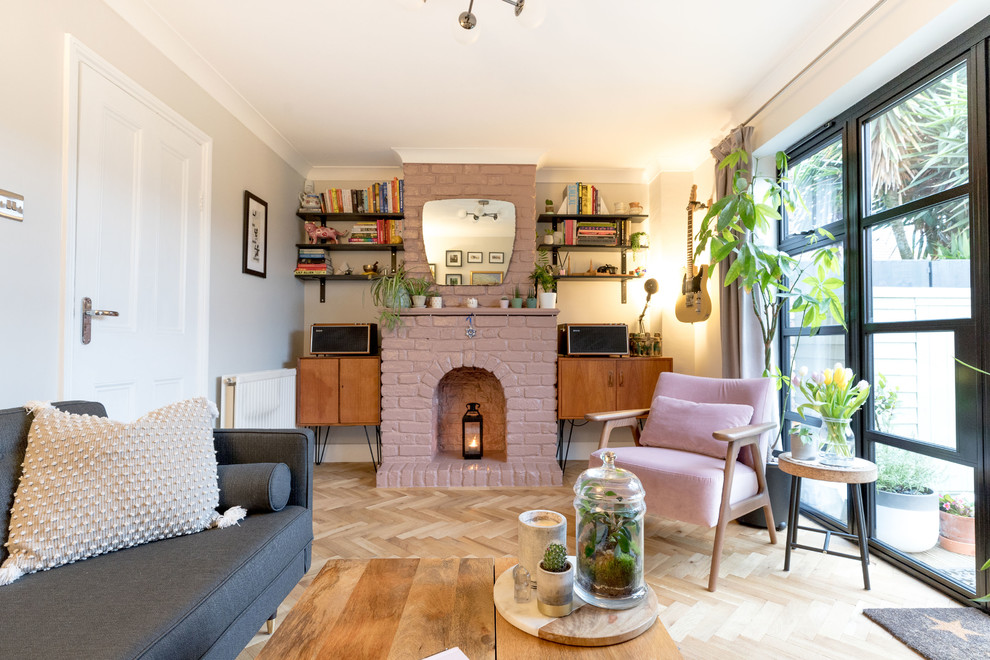 Mid-sized transitional enclosed living room in London with pink walls, a standard fireplace, a brick fireplace surround, medium hardwood floors, a freestanding tv and brown floor.