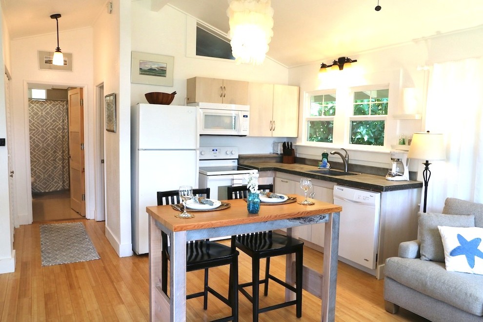 This is an example of a small beach style l-shaped open plan kitchen in Hawaii with an undermount sink, flat-panel cabinets, distressed cabinets, concrete benchtops, grey splashback, timber splashback, white appliances, bamboo floors, grey benchtop, no island and yellow floor.