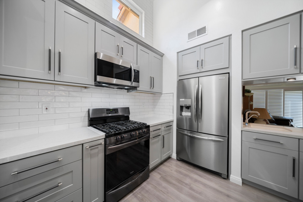 Kitchen - modern vinyl floor and brown floor kitchen idea in Orange County with an undermount sink, shaker cabinets, gray cabinets, quartz countertops, white backsplash, black appliances and white countertops