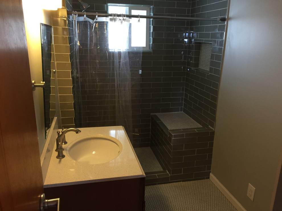 Photo of a small modern master bathroom in Indianapolis with an integrated sink, raised-panel cabinets, medium wood cabinets, engineered quartz benchtops, an open shower, a two-piece toilet, gray tile, glass tile, grey walls and mosaic tile floors.