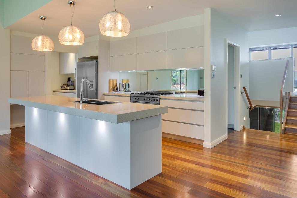 Contemporary galley kitchen in Sydney with an undermount sink, white cabinets, mirror splashback, stainless steel appliances, medium hardwood floors and with island.