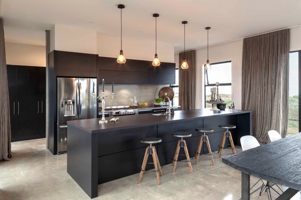 Photo of a contemporary galley kitchen in Other with an undermount sink, flat-panel cabinets, black cabinets, grey splashback, stainless steel appliances, concrete floors, with island and grey floor.