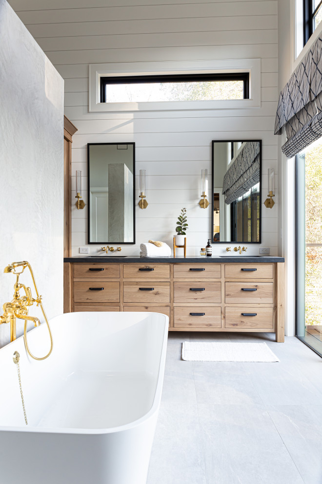 This is an example of a large farmhouse ensuite bathroom in San Francisco with flat-panel cabinets, light wood cabinets, a freestanding bath, white walls, porcelain flooring, a submerged sink, granite worktops, grey floors, black worktops, double sinks and a built in vanity unit.