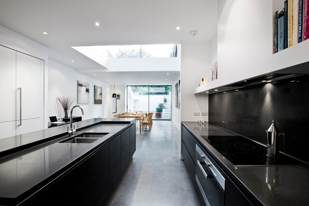 Photo of a contemporary eat-in kitchen in London with with island, a double-bowl sink, flat-panel cabinets, black cabinets, black splashback and concrete floors.