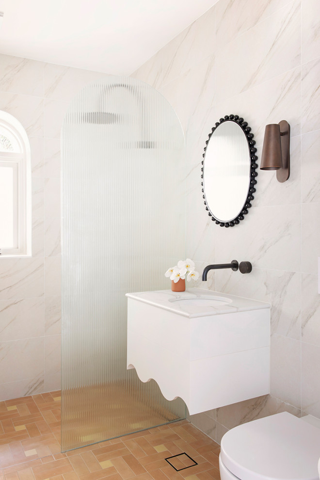 Idées déco pour un WC suspendu méditerranéen avec des portes de placard blanches, un carrelage blanc, un mur blanc, un sol en carrelage de porcelaine, un lavabo encastré, un plan de toilette en marbre, un sol marron et meuble-lavabo suspendu.