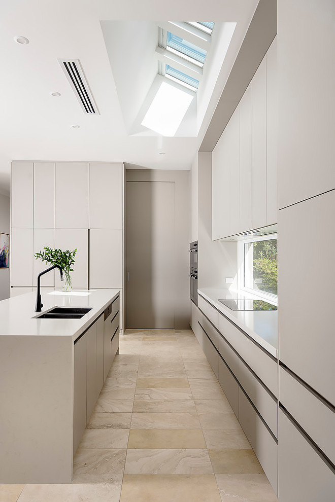 This is an example of a large contemporary galley open plan kitchen in Perth with an undermount sink, grey cabinets, quartz benchtops, window splashback, stainless steel appliances, travertine floors, with island and beige floor.