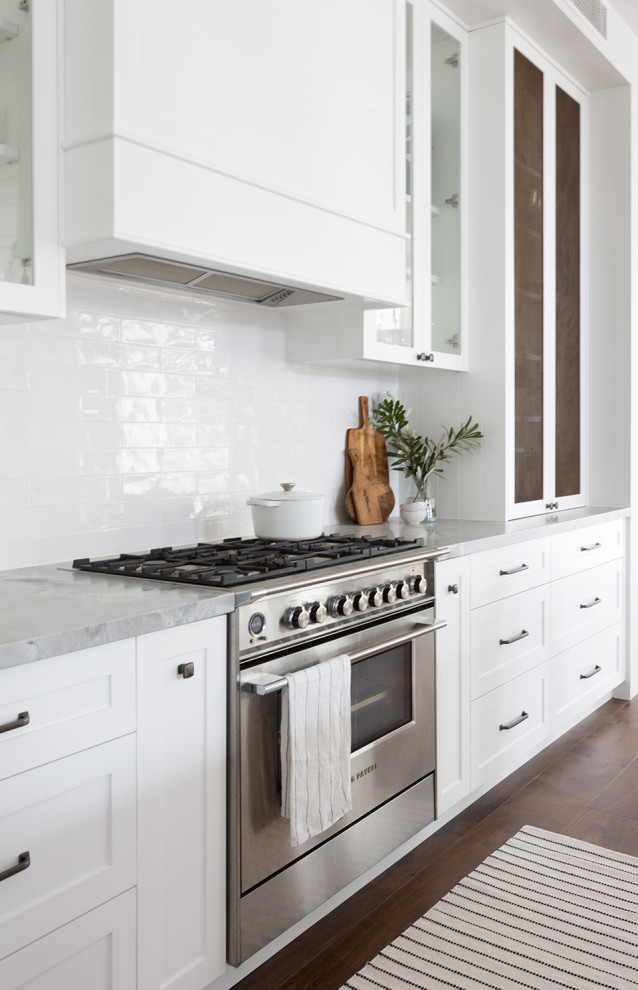 This is an example of a large traditional galley open plan kitchen in Sydney with a double-bowl sink, shaker cabinets, white cabinets, marble benchtops, white splashback, ceramic splashback, stainless steel appliances, dark hardwood floors, with island, brown floor, grey benchtop and recessed.