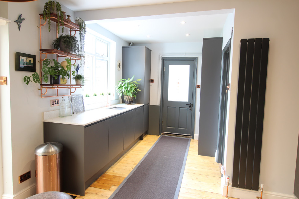 Photo of a mid-sized contemporary l-shaped kitchen in Cambridgeshire with flat-panel cabinets, grey cabinets, quartzite benchtops, multi-coloured splashback, ceramic splashback, light hardwood floors and white benchtop.