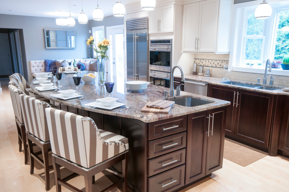 Photo of an expansive transitional l-shaped open plan kitchen in Providence with with island, shaker cabinets, white cabinets, granite benchtops, beige splashback, stone tile splashback, stainless steel appliances, an undermount sink and light hardwood floors.