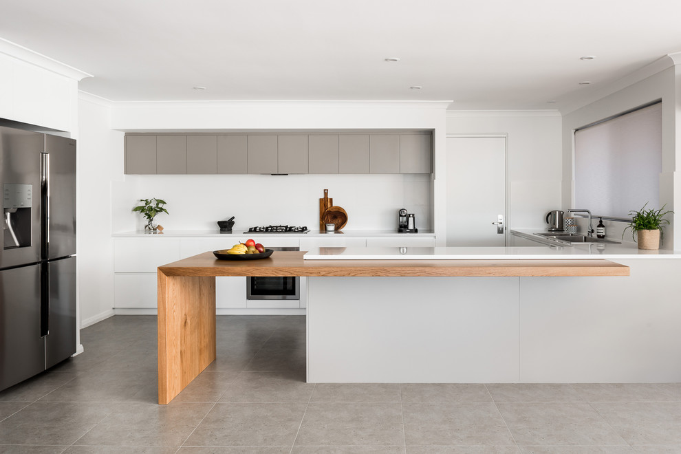 This is an example of a large modern galley kitchen in Perth with a drop-in sink, flat-panel cabinets, white cabinets, quartz benchtops, white splashback, porcelain splashback, stainless steel appliances, porcelain floors, with island and grey floor.