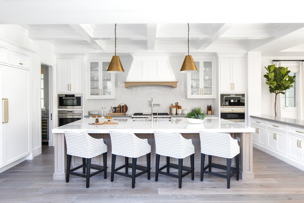 Beach style kitchen in Los Angeles with an undermount sink, white cabinets, white splashback, light hardwood floors, with island, panelled appliances and shaker cabinets.