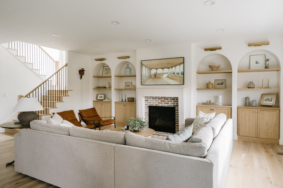 This is an example of a mid-sized transitional formal open concept living room in Salt Lake City with white walls, light hardwood floors, a standard fireplace, a stone fireplace surround, a wall-mounted tv and brick walls.