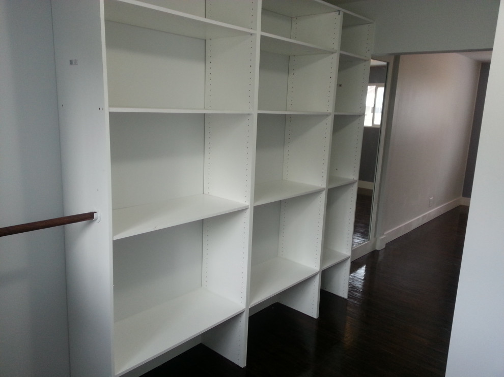 Photo of a large urban walk-in wardrobe in Calgary with open cabinets, white cabinets, dark hardwood flooring and brown floors.